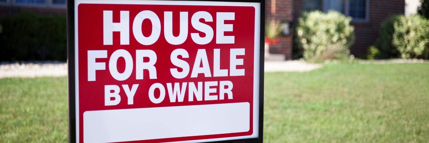 House for Sale By Owner sign on a lawn in front of a house