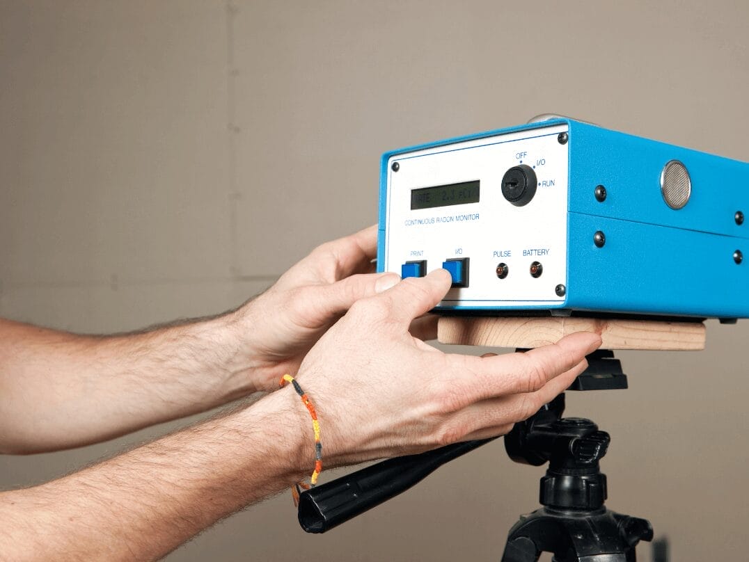 A close-up of hands adjusting a continuous radon monitor used for home radon testing.